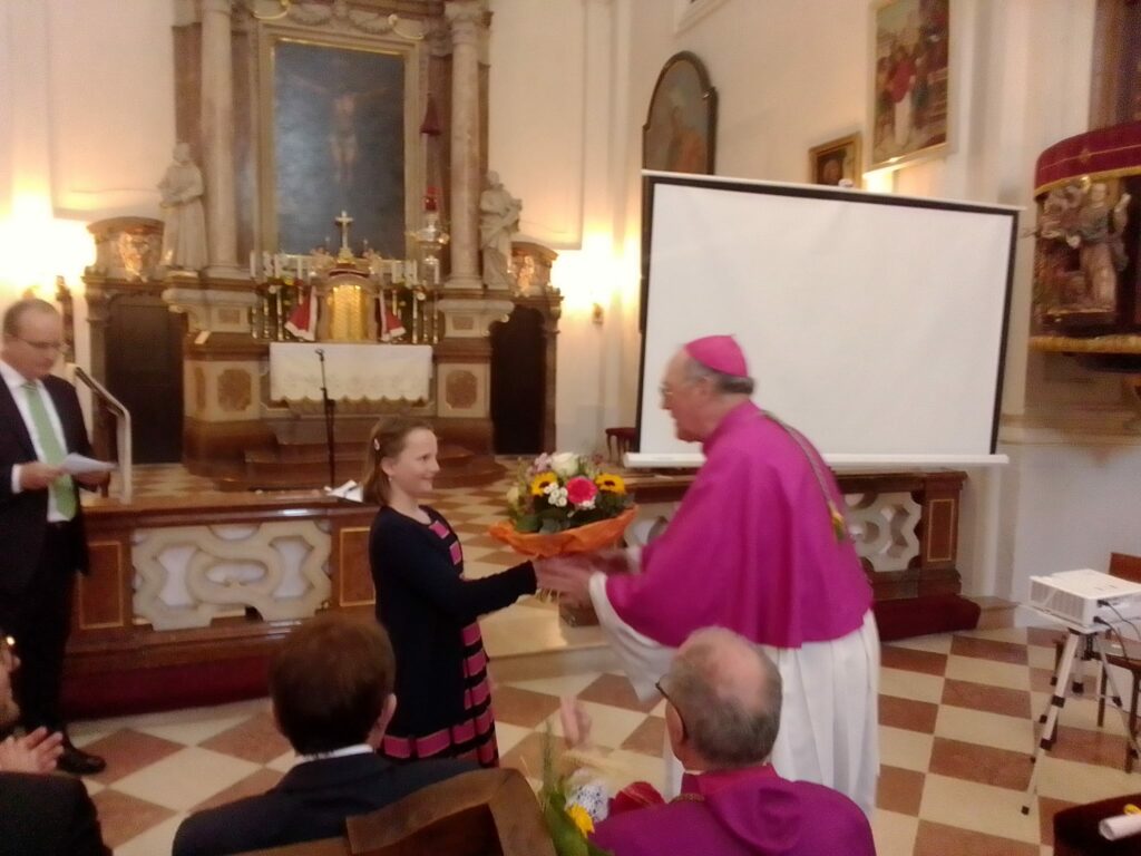 Ein Mädchen überreicht dem Diözesanbischof Blumen